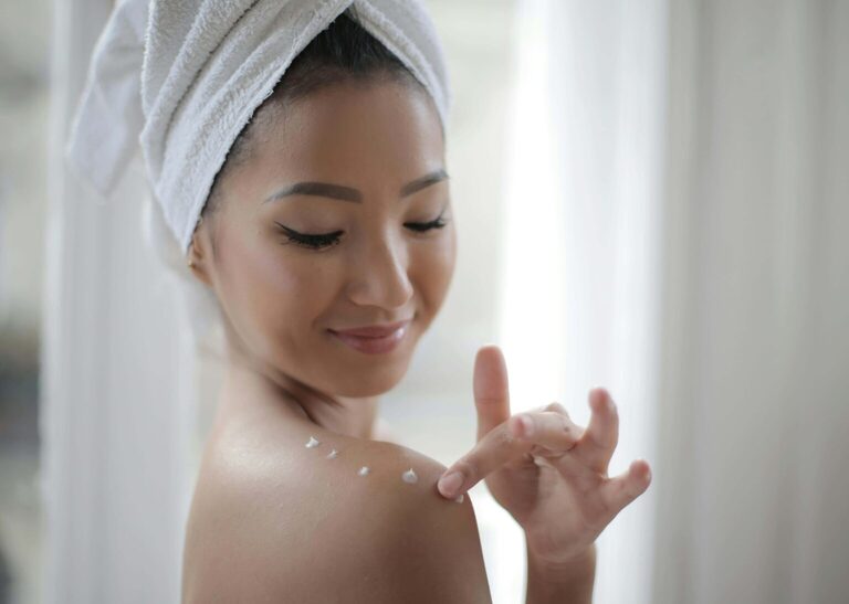 happy young woman applying body lotion to her shoulder. What is an everything shower meaning everything shower. Everything shower list. everything shower routine. everything shower meaning. luxury shower. luxury shower routine.