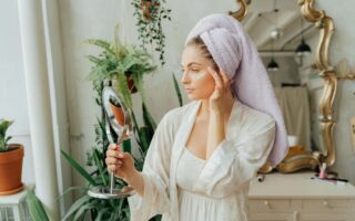 Beautiful woman looking into a hand mirror in the bathroom. best at home facial kit. Self care sunday. diy face mask. diy facial at home. at home facial steps. at home facial steamer. Best facial for glowing skin. how to get radiant skin.