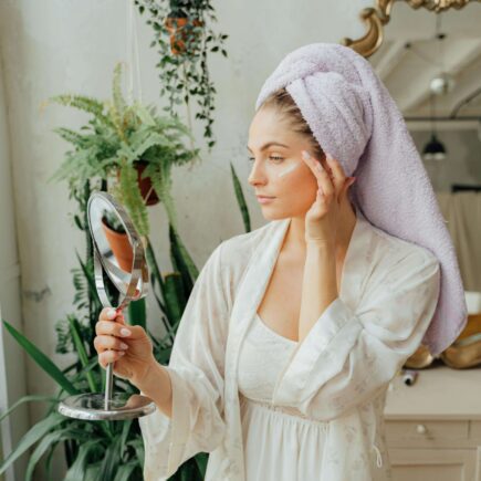 Beautiful woman looking into a hand mirror in the bathroom. best at home facial kit. Self care sunday. diy face mask. diy facial at home. at home facial steps. at home facial steamer. Best facial for glowing skin. how to get radiant skin.