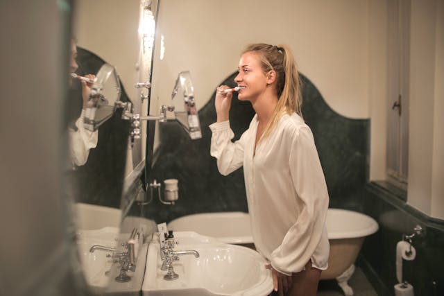 woman brushing her teeth in the mirror. Morning routine ideas. morning routine checklist. how to create a morning routine. how to start a morning routine. what is the best morning routine.