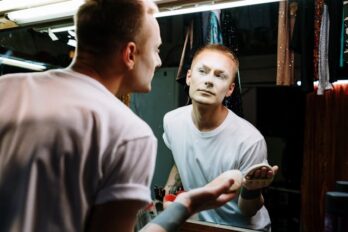 man in theatre dressing room looking at his makeup in the mirror. Best foundation. how to apply powder foundation. How to choose makeup foundation. Makeup foundation types. Makeup foundation tips. Types of foundation makeup. what is foundation makeup.