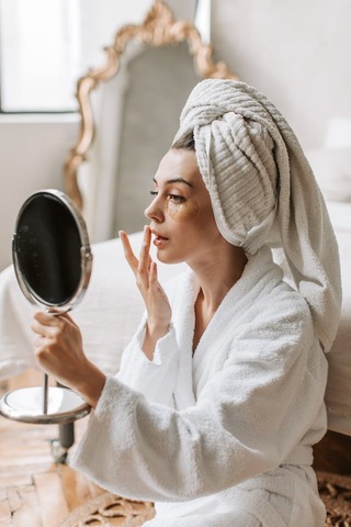 woman wearing under eye masks looking in a mirror pplying lip balm after the shower. Best foundation. how to apply powder foundation. How to choose makeup foundation. Makeup foundation types. Makeup foundation tips. Types of foundation makeup. what is foundation makeup.