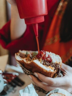 close up of ketchup being added to a half eaten burger. Hangover breakfast ideas. hangover skin. how to fix a hangover quick. how to treat dehydrated skin. how to fix dehydrated skin. tired when hungover. re energize.