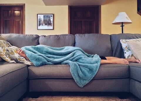 person lying on the couch covering their face with a blanket. Hangover breakfast ideas. hangover skin. how to fix a hangover quick. how to treat dehydrated skin. how to fix dehydrated skin. tired when hungover. re energize.