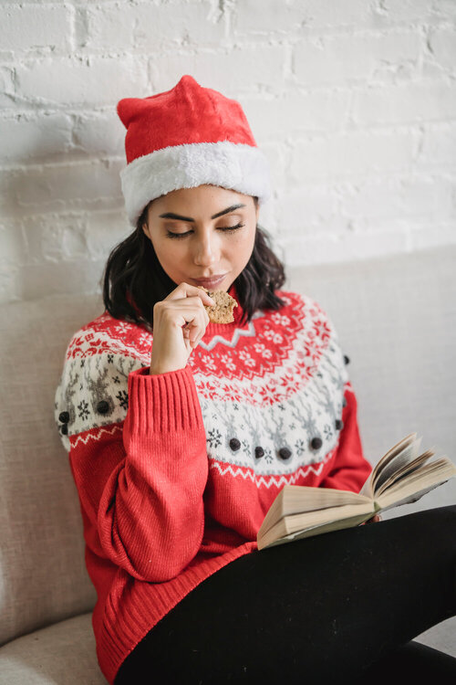 young woman in christmas clothes reading a book at home. Surviving Christmas. Surviving Christmas. Self care and how to glow up. New Year's Eve. christmas self care. Stress-free Christmas season.