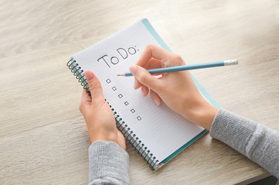 Close up of a womans hands holding a pencil and a notepad, writing a 'to do' list. Surviving Christmas. Surviving Christmas. Self care and how to glow up. New Year's Eve. christmas self care. Stress-free Christmas season.